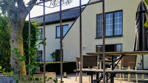 A patio area with outdoor furniture, a pergola, and a building in the background. - Hotel Lepelbed Melle (Melle)