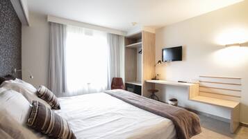 Ein modernes Hotelzimmer mit einem großen Bett, einem an der Wand montierten Fernseher, einem Schreibtisch und einem Kleiderschrank.