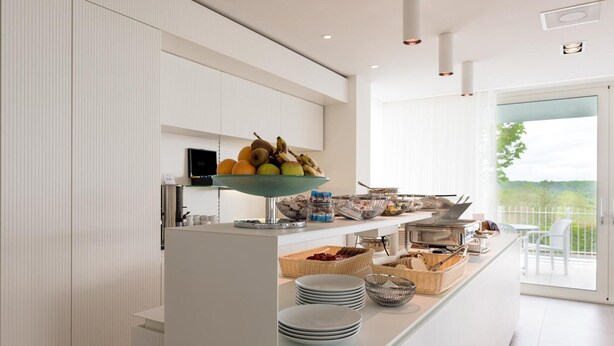 Una cocina moderna con armarios blancos, un frutero y un espacio tipo bufé con platos y cestas.