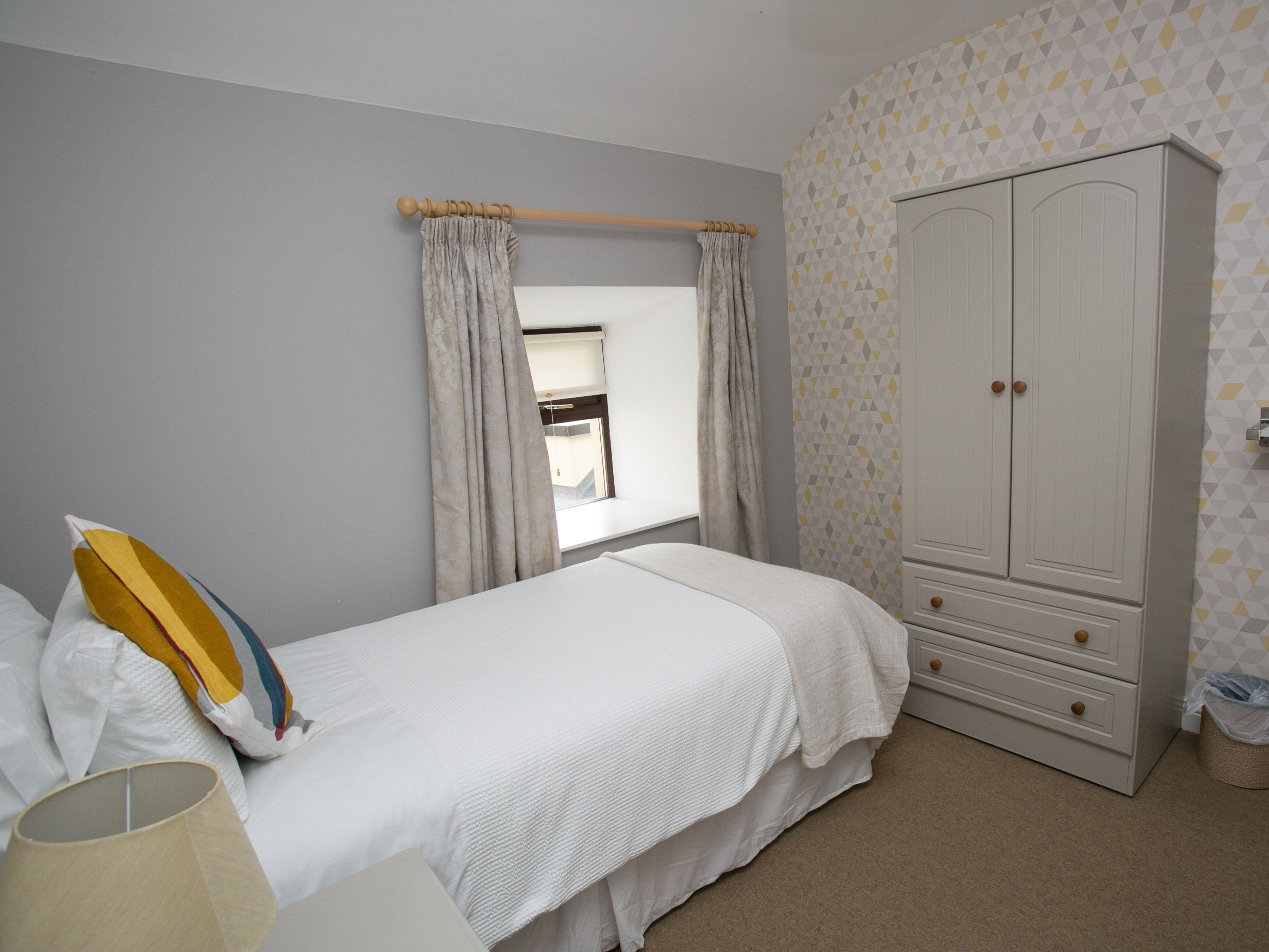 A bedroom with a bed, a wardrobe, and a window with curtains.