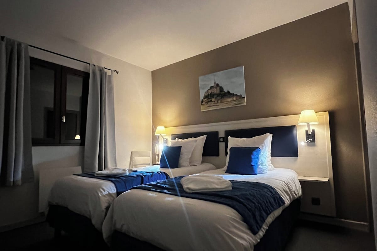 A hotel room with a large bed, two bedside tables, a window with curtains, a wall-mounted painting, and a ceiling light.