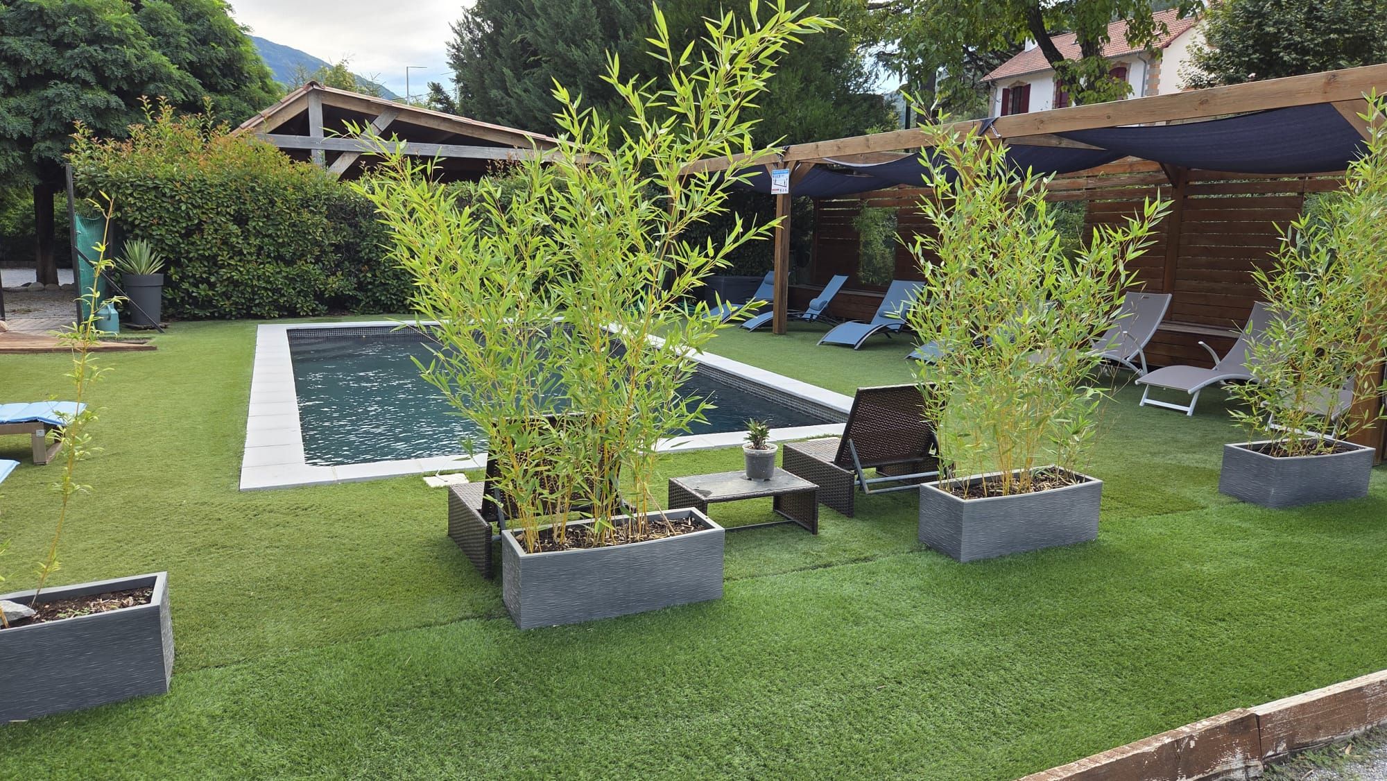Um quintal com piscina, grama sintética e várias plantas em vasos.