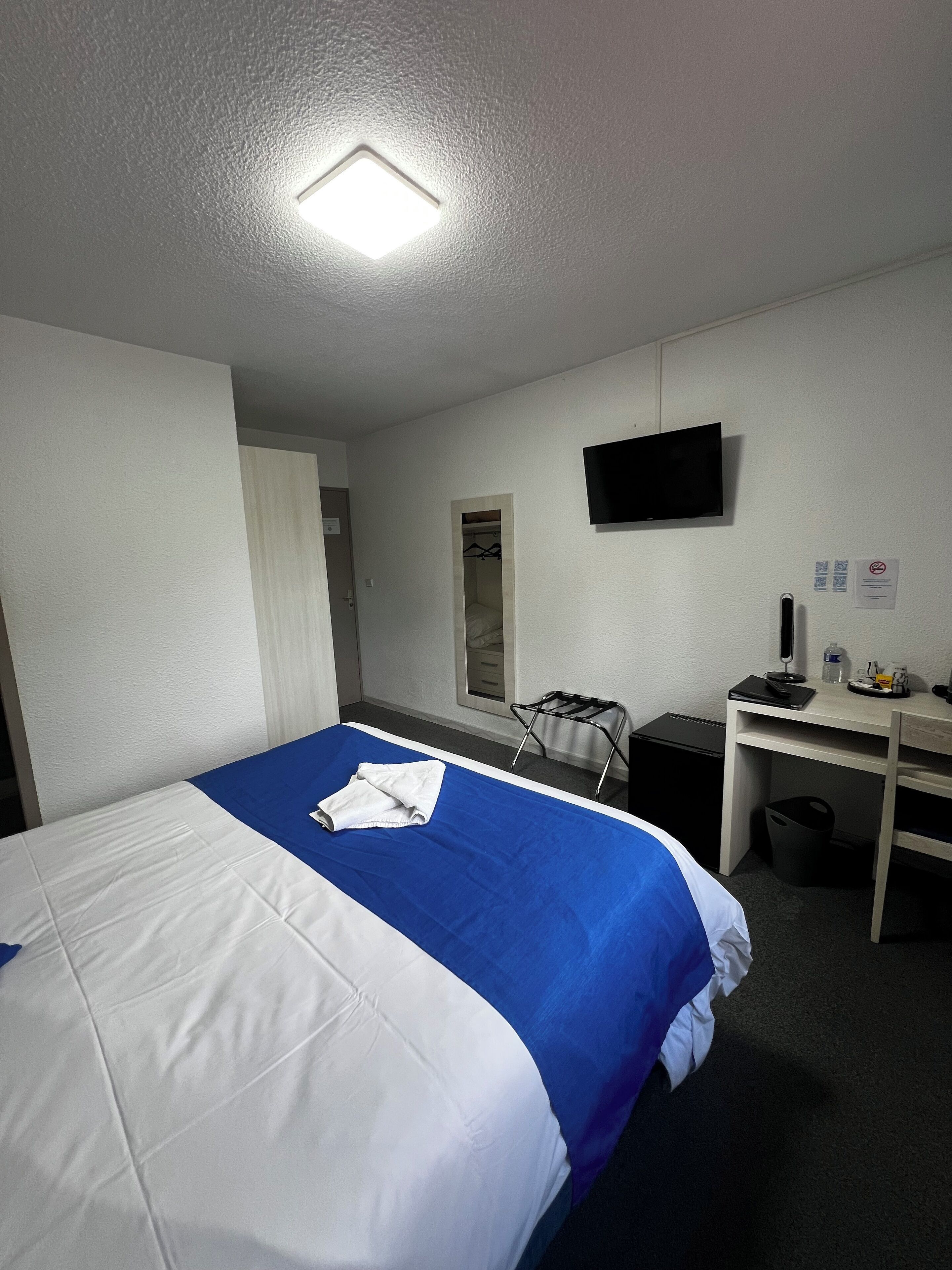 Una habitación de hotel con una cama, un escritorio, un televisor y un pequeño cubo de basura.