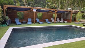 A rectangular swimming pool with a tiled edge, surrounded by a wooden deck. There are multiple lounge chairs aligned along the poolside. - Hotel Les Alizés (Puget-Theniers)