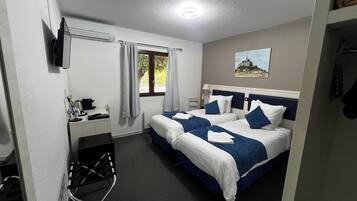 Habitación de hotel con dos camas, un escritorio, una silla, un televisor, un cuadro y una ventana con cortinas.