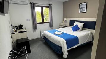 Et hotelværelse med seng, skrivebord, stol og et vindue med gardiner.