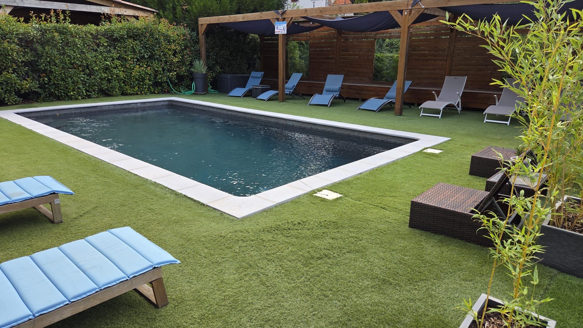 A rectangular swimming pool with a surrounding deck, lounge chairs, and artificial grass.