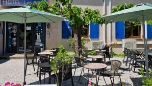 Un hotel con mesas al aire libre, contraventanas azules y un letrero que dice "HOTEL Les Arcs".