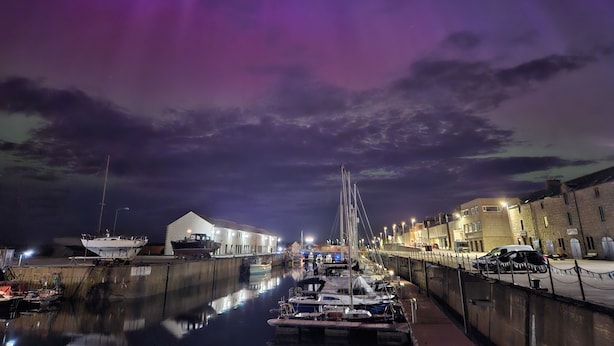 Un port de plaisance de nuit, avec des bateaux amarrés, un bâtiment sur la gauche et une rue sur la droite.