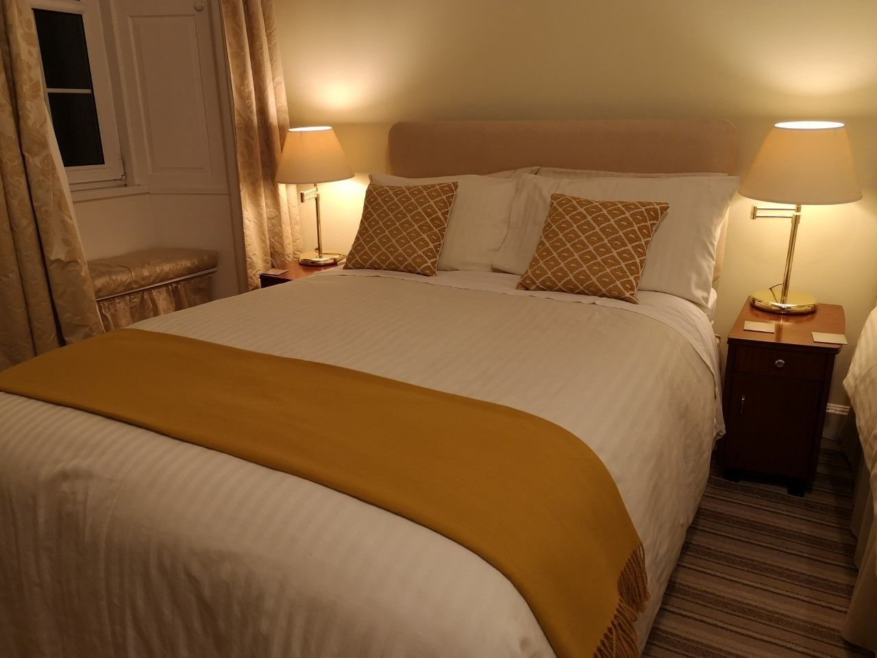A neatly made bed with a yellow throw blanket, two bedside lamps, and a small wooden nightstand.