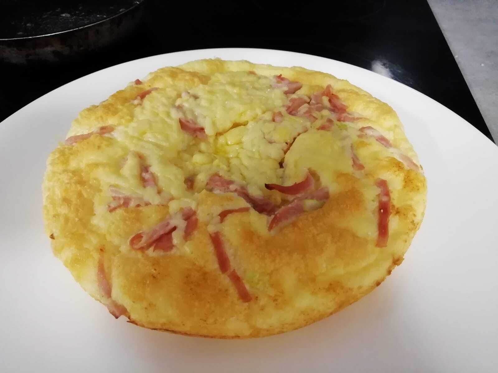 Ein runder Teller mit einer goldbraunen Kruste, vermutlich ein herzhafter Pfannkuchen oder eine Art Omelett.