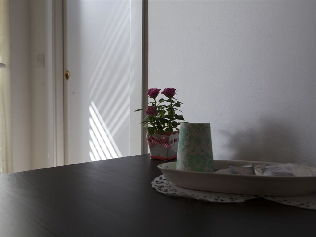 A dark wooden table with a white plate, a green and white vase with flowers, and a white box with a red ribbon.