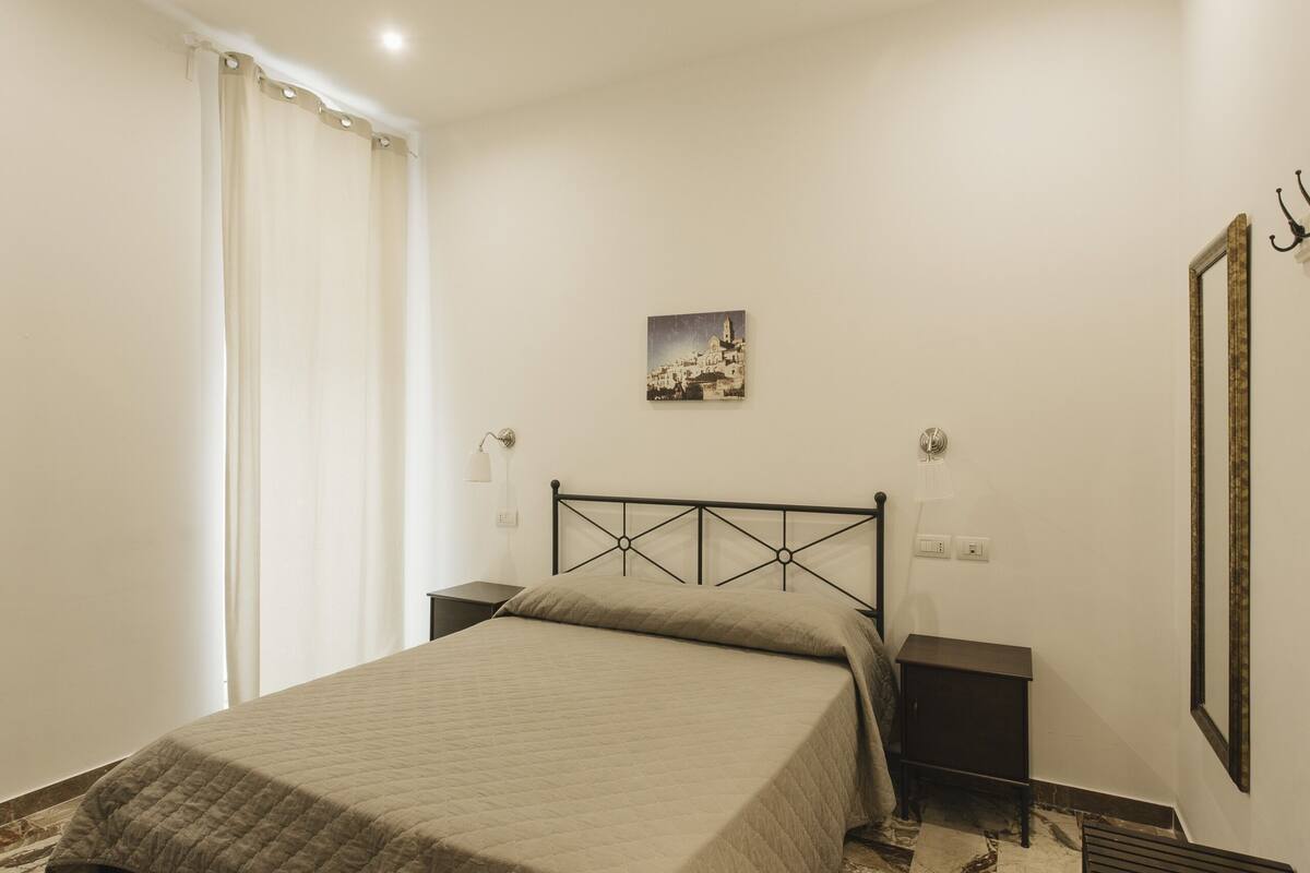 Une chambre à coucher comprenant un lit, des tables de chevet, une commode, une lampe fixée au mur, un tableau et un miroir.