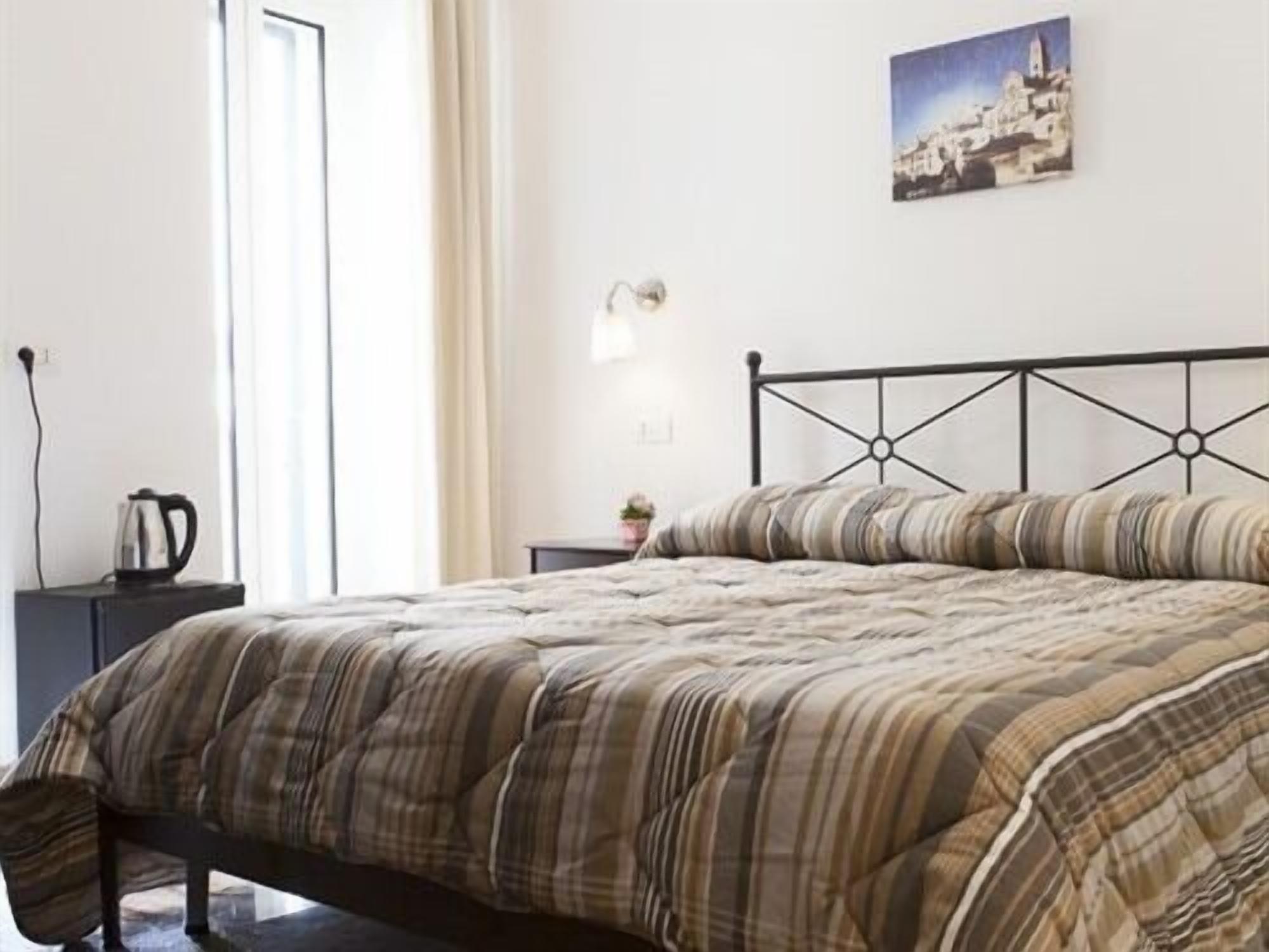 Un lit avec une couvre-lit à rayures, une table de chevet avec une bouilloire et un tableau accroché au mur.