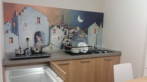 Et køkken med et muralmaleri af en by, en komfur, en vask og et køleskab.