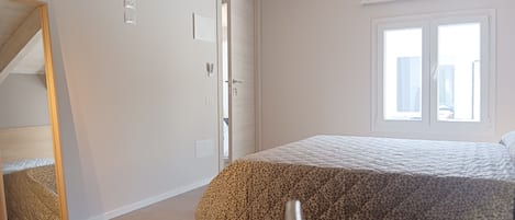 A bedroom with a bed, a window, a door, and a mirror.