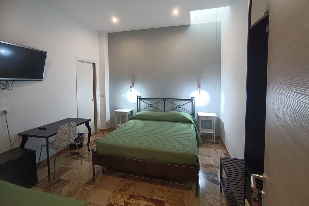 Une chambre à coucher comprenant un lit, un bureau, une chaise, un téléviseur et deux lampes de chevet.