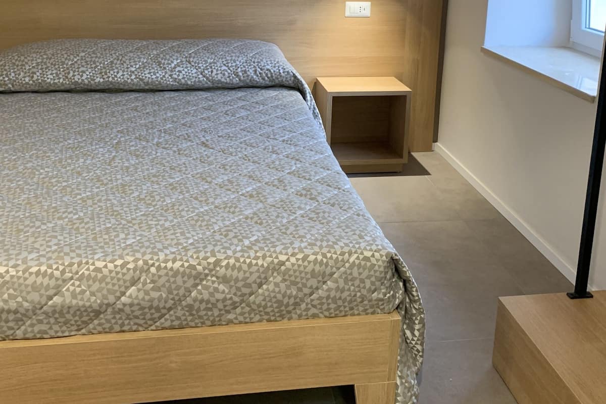Une chambre à coucher avec un lit en bois, une table de chevet, une commode, une lampe suspendue et une fenêtre donnant sur un beau paysage.
