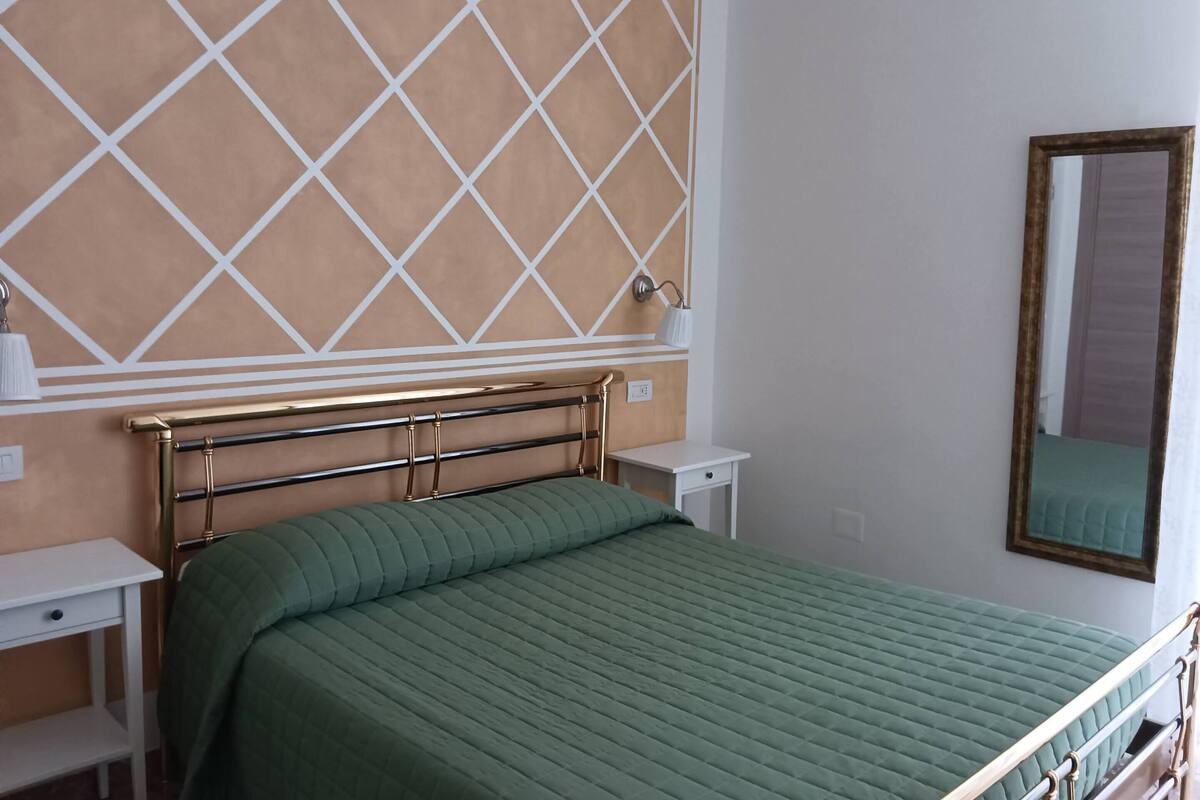 Une chambre à coucher bien rangée, avec un lit, des tables de chevet et un miroir fixé au mur.