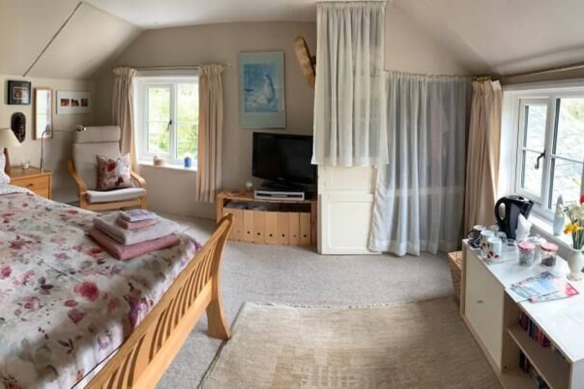 Une chambre à coucher comprenant un lit, des tables de chevet, un bureau, une chaise, un téléviseur et une fenêtre avec des rideaux.