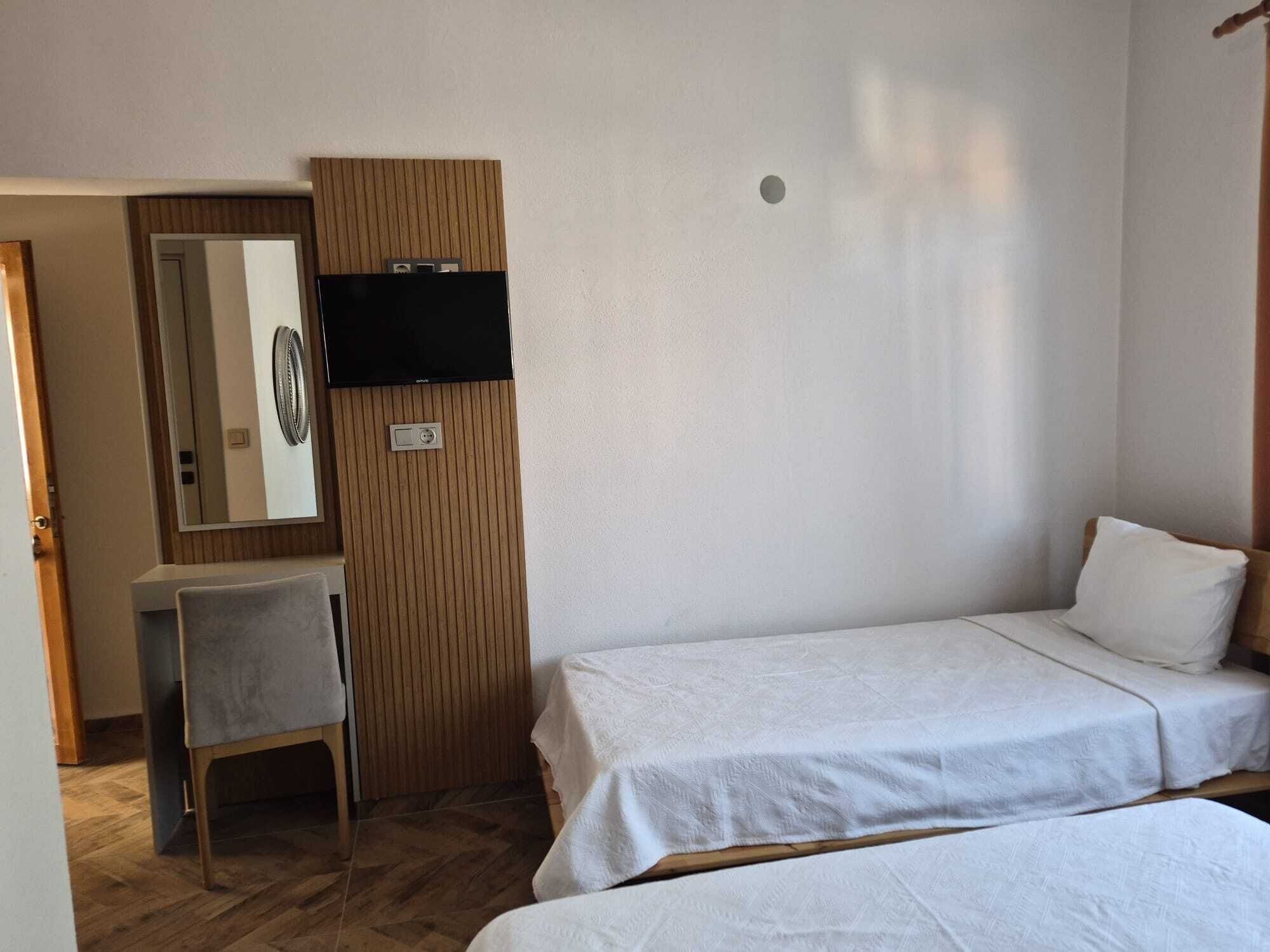 Une chambre avec deux lits, un bureau, une chaise, un téléviseur fixé sur un panneau en bois et une porte.