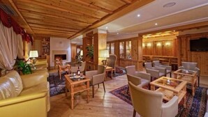 Un hall d’hôtel spacieux, doté d’un plancher en bois, d’une cheminée et d’un espace détente avec de nombreux fauteuils et tables.