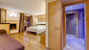 Une chambre d’hôtel moderne avec un plancher en bois, un lit avec du linge de maison blanc, un petit coin salon et une cheminée.