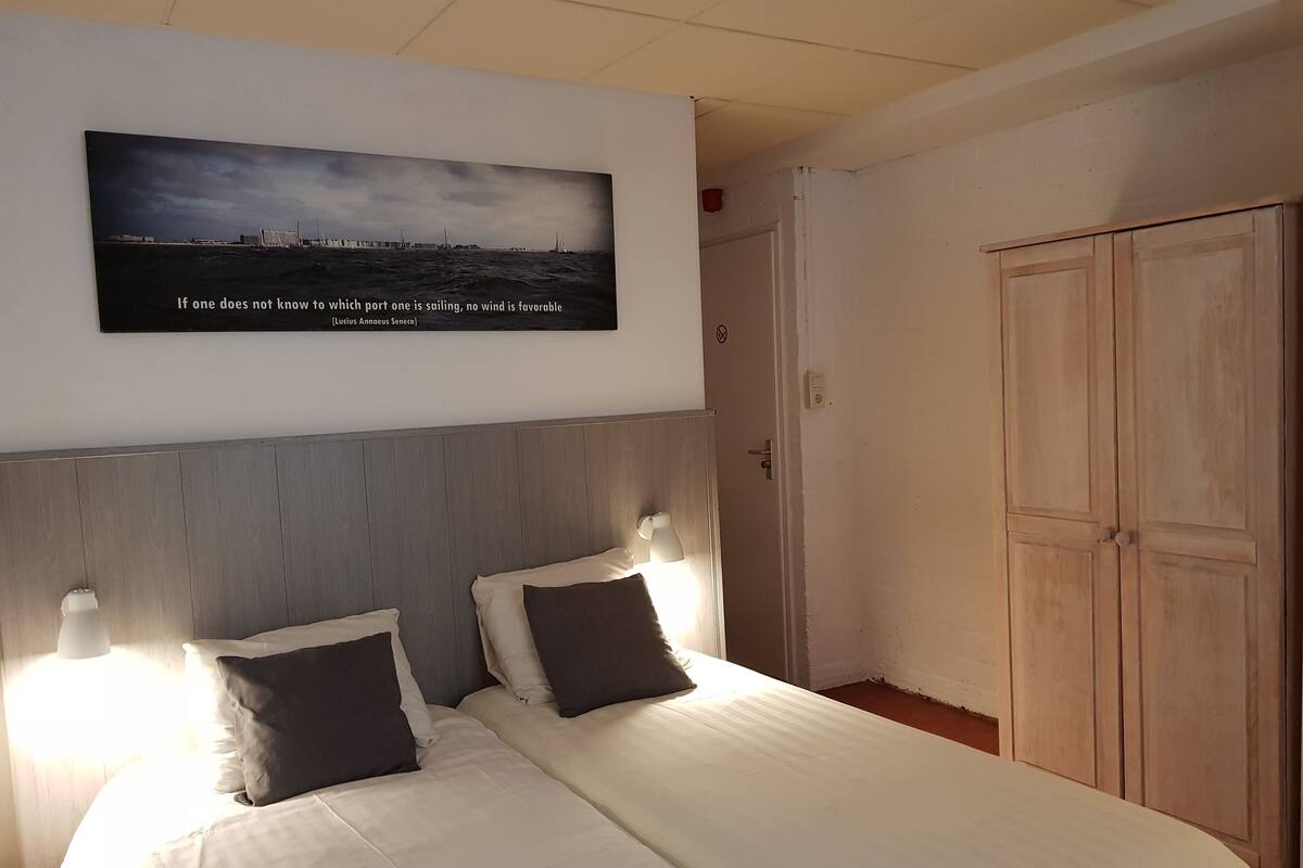 A neatly made bed with two pillows, a wooden headboard, and a wall-mounted picture of a harbor scene.