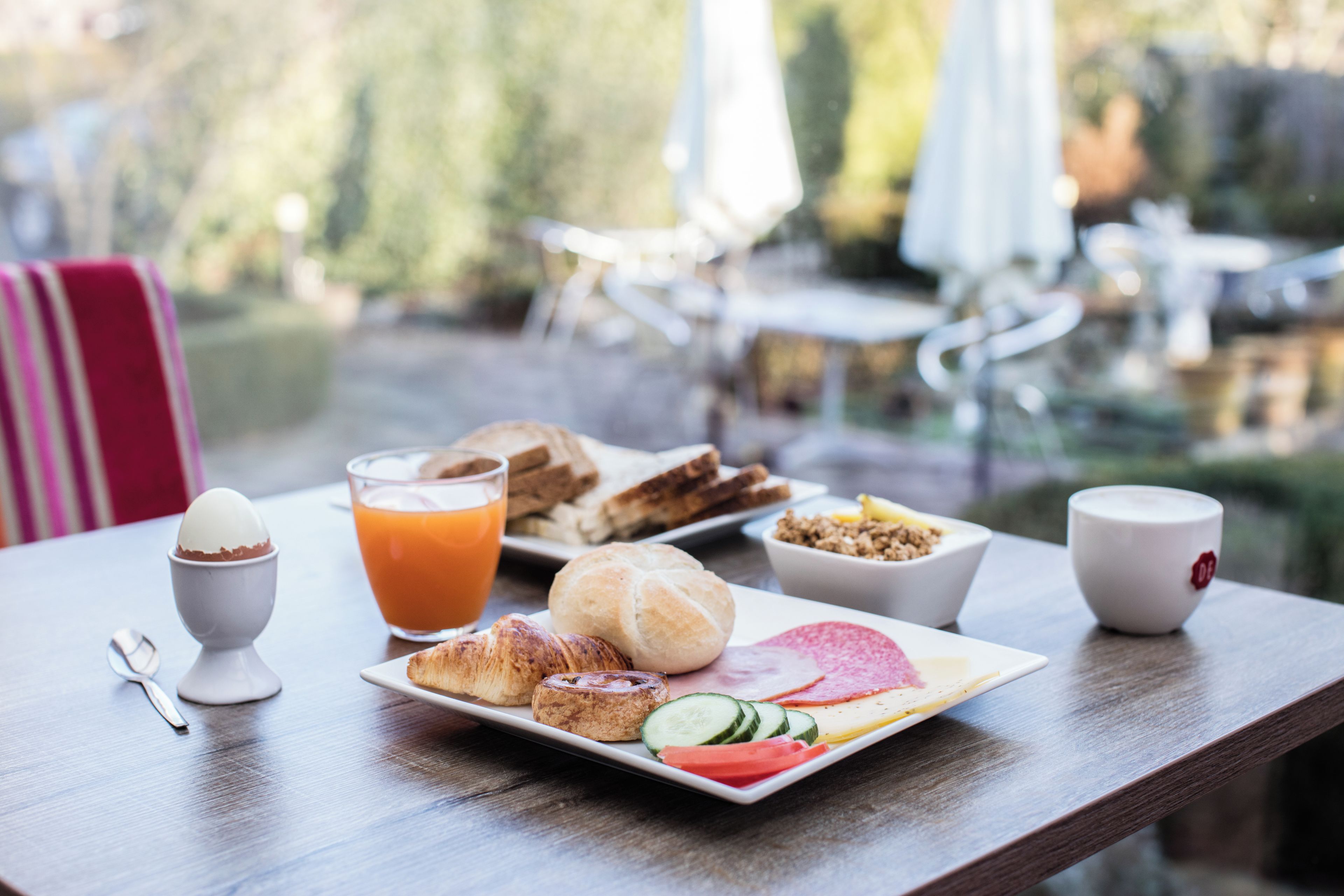 An outdoor dining table with breakfast items including eggs, toast, croissants, and a fruit plate.