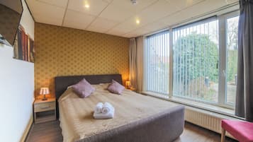 Een hotelkamer met een groot bed, twee bedlampen, een raam met zonwering en uitzicht op groen.