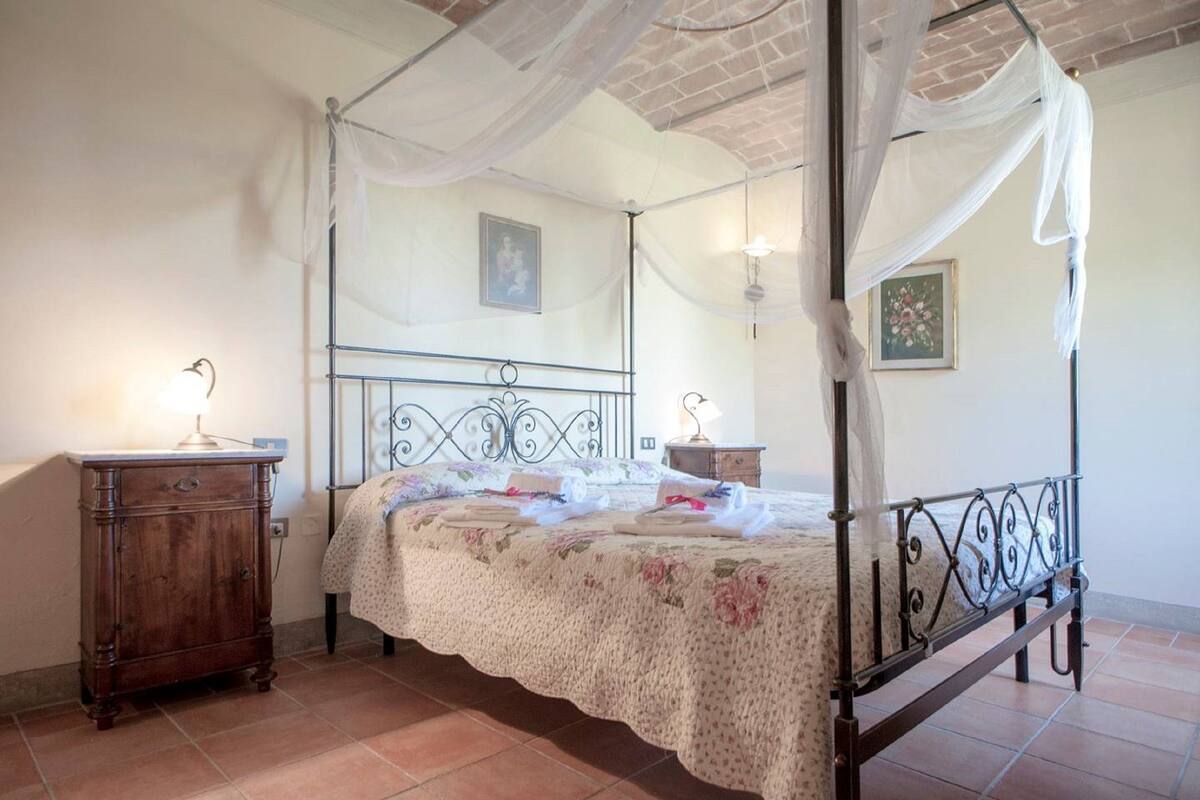 Un lit à baldaquin, une table de chevet en bois et une lampe fixée au mur.