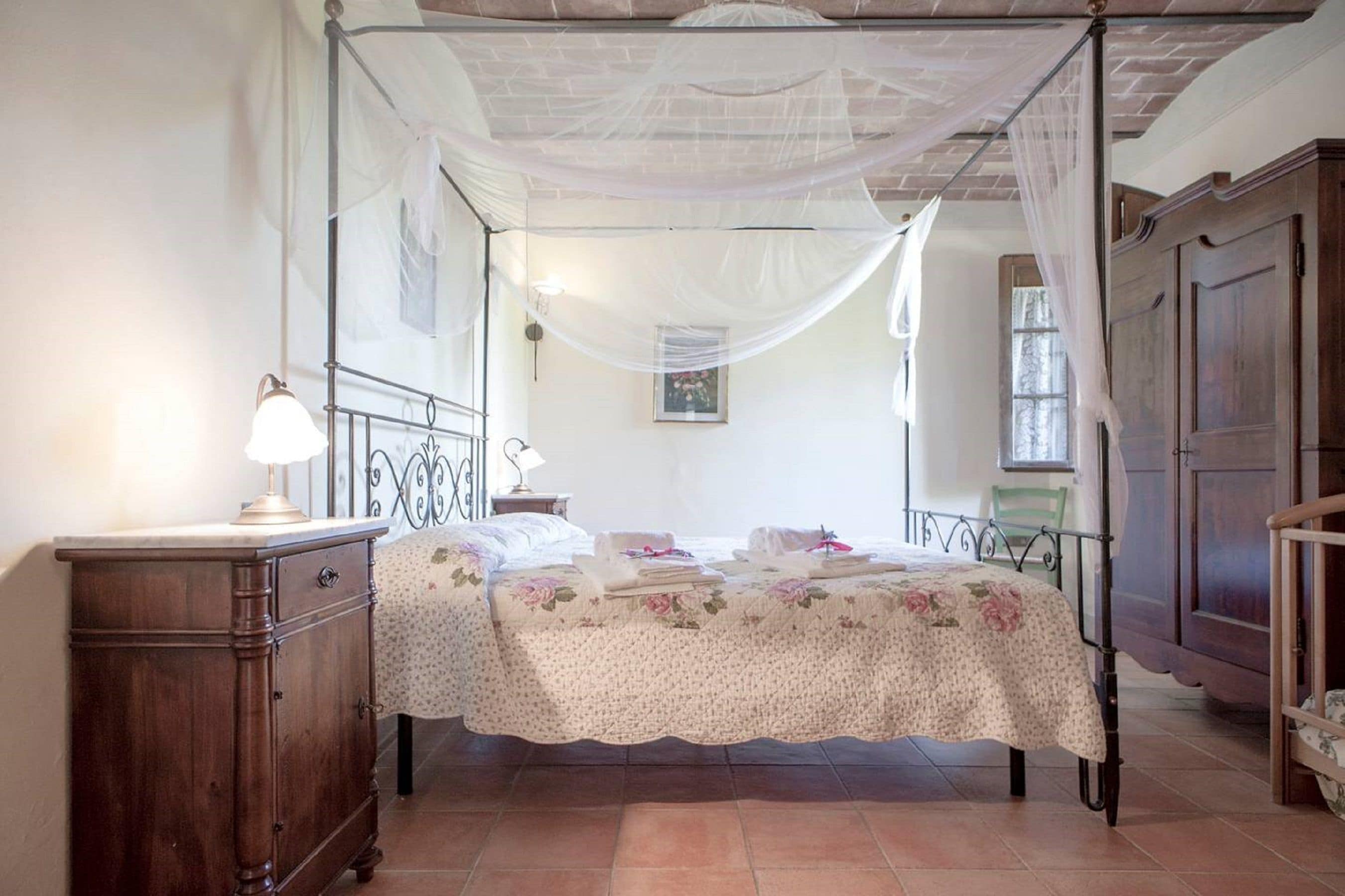 Quarto com cama de dossel, cómoda de madeira e cortina sobre a cama.