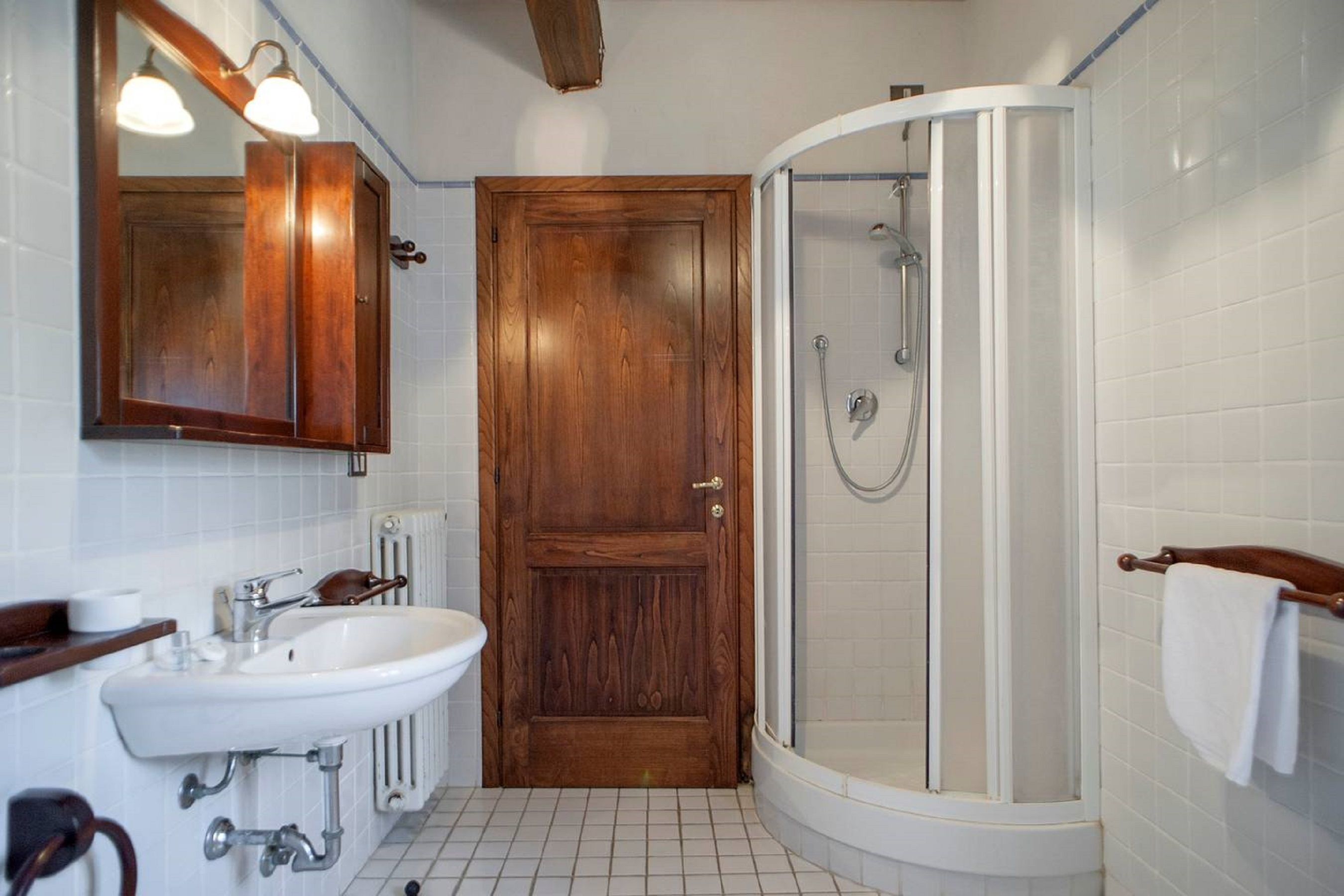 A bathroom with a wooden door, a white sink, a mirror, and a glass-enclosed shower.