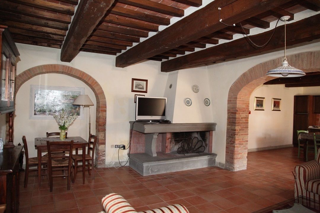 A living room with a fireplace, wooden beams, a television, and a dining area with chairs and a table.