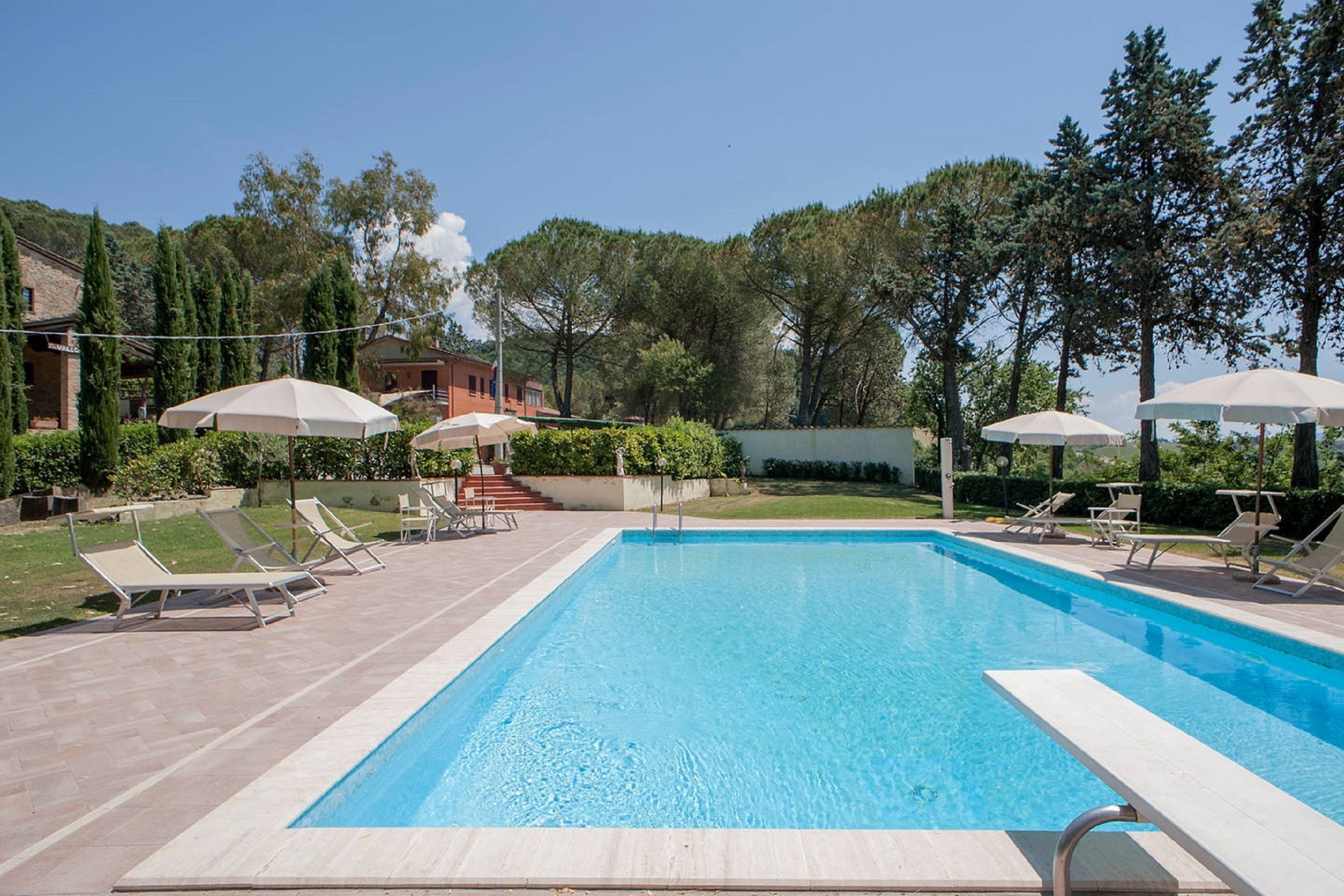 A rectangular swimming pool with a tiled deck, surrounded by lounge chairs and umbrellas.