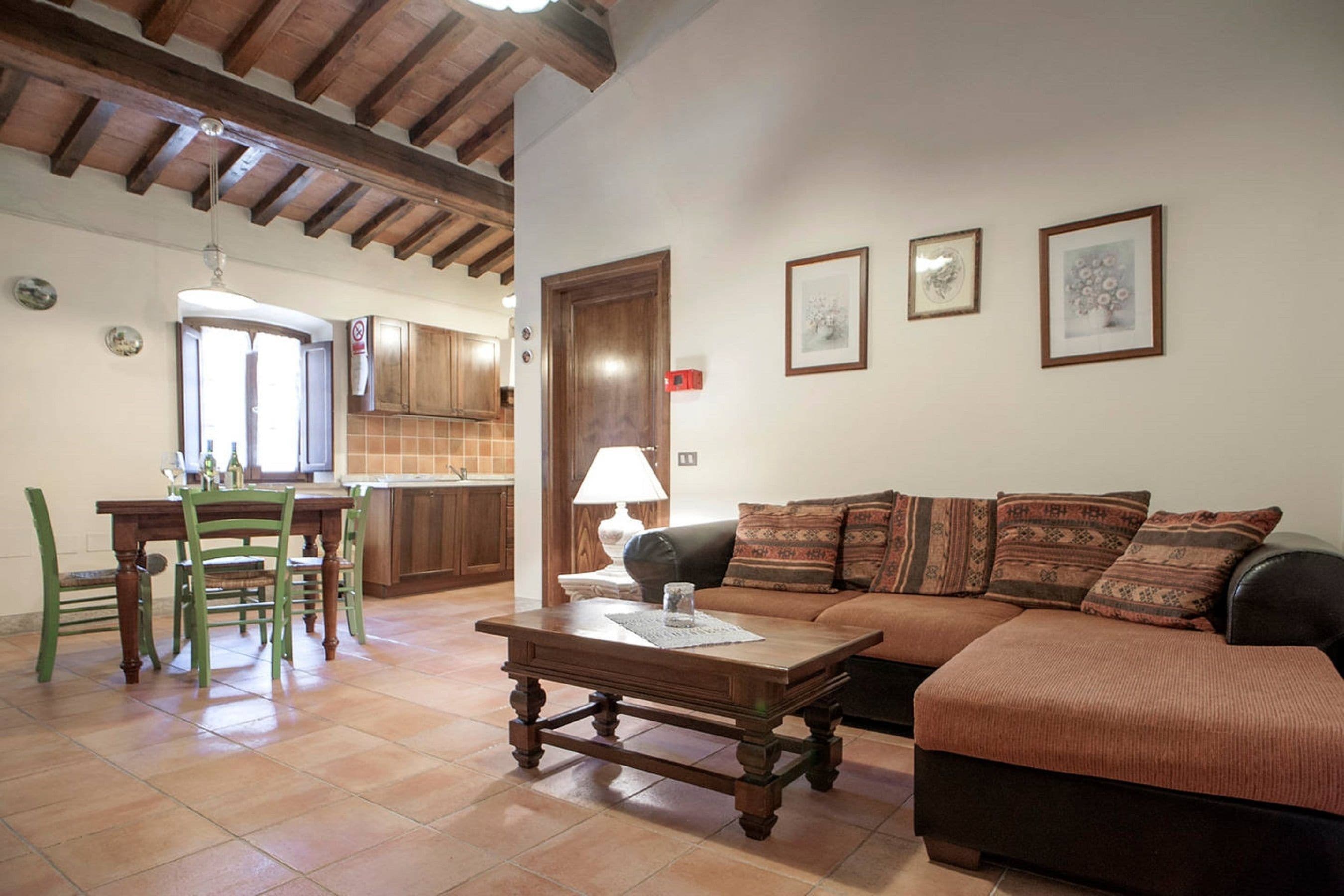 A living room with a wooden coffee table, a sofa with patterned cushions, and a dining area with green chairs.