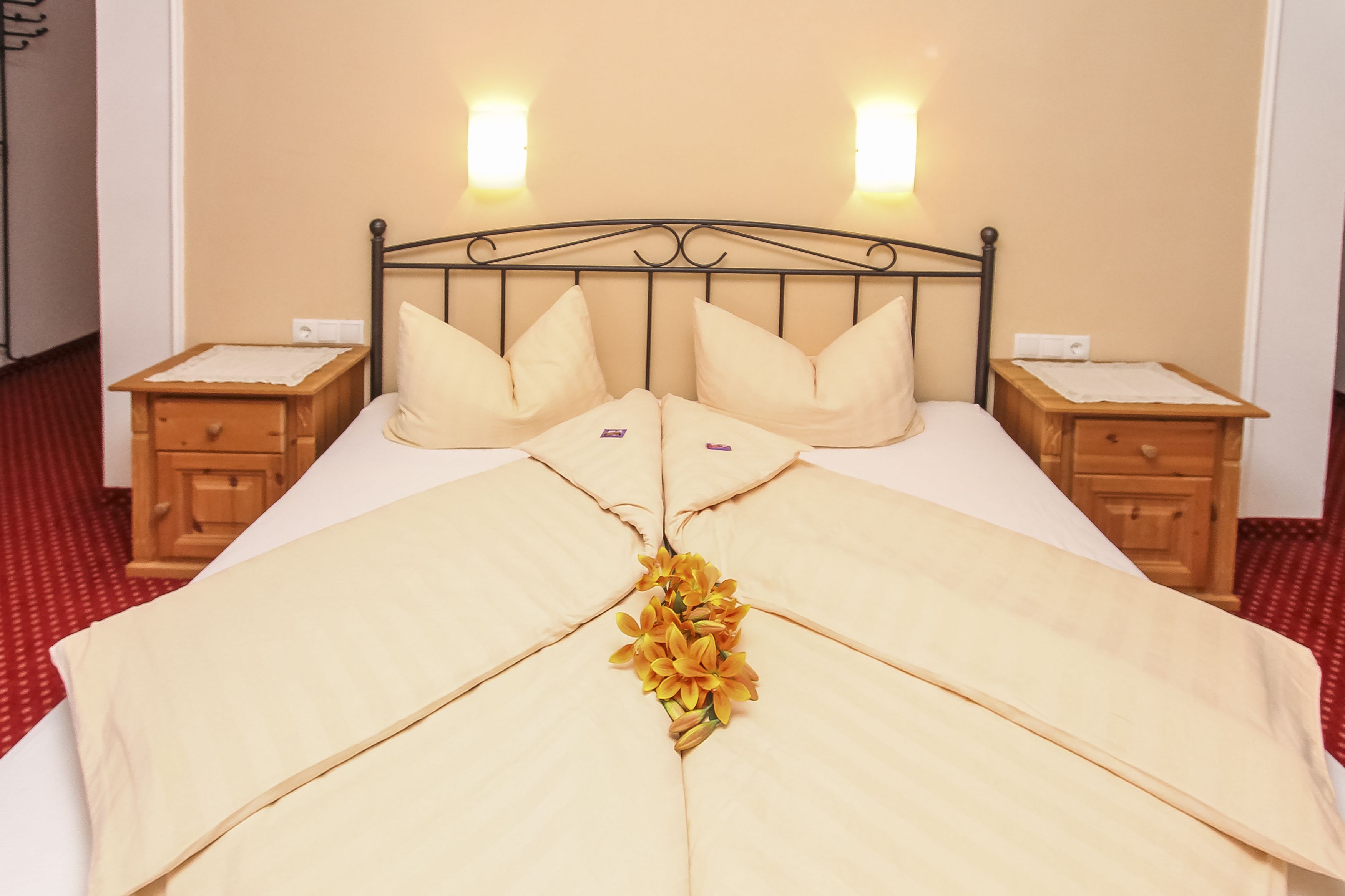 Una cama impecablemente arreglada con un arreglo floral decorativo en el centro, flanqueada por dos mesitas de noche con lámparas.