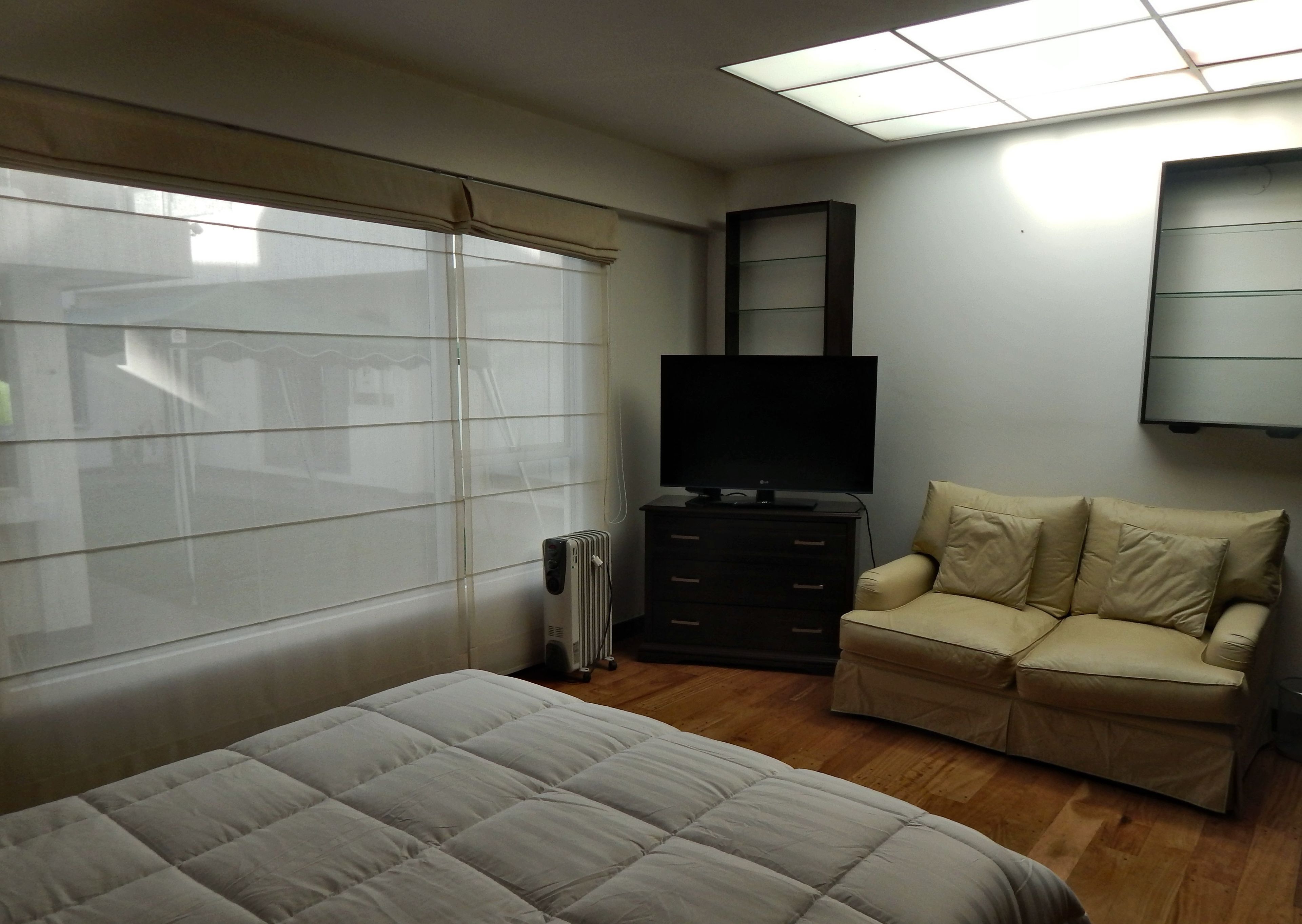 A bedroom with a bed, a TV on a dresser, a chair, and a radiator.