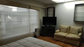 A bedroom with a bed, a TV on a dresser, a chair, and a radiator.