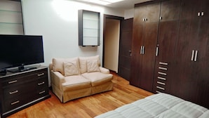 Un dormitorio con cama, sofá, televisión, armario y espejo.