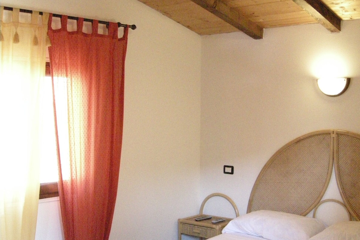A bedroom with a large bed, a nightstand, a lamp, and a window with curtains.