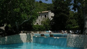 A pool with a waterfall feature, surrounded by stone walls and potted plants. - A' Cunziria (Vizzini)