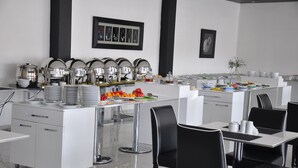 A modern dining area with white tables and black chairs, a buffet with various food items, and a clean, minimalist design. - Kayseri Kosk Otel (Kayseri)