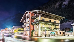 A multi-story hotel with balconies, a snow-covered street, and a mountainous backdrop. - B&B Oberreiter (Fusch an der Grossglocknerstrasse)