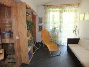 A room with a wooden cabinet, a yellow chair, a sofa, and a window with curtains. - B&B Oberreiter (Fusch an der Grossglocknerstrasse)