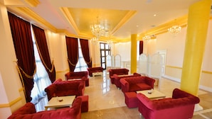 A hotel lobby with red upholstered sofas arranged around a central coffee table, a chandelier, and a large mirror. - Hotel Luani Arte (Shkodër)