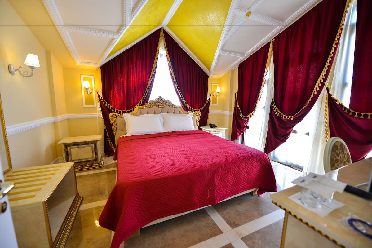 Habitación de hotel con una cama grande, un escritorio y una silla. Hay cortinas y una lámpara en la pared.