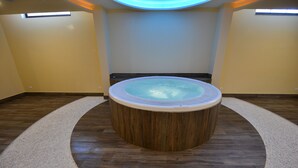 A circular hot tub with a wooden base and a glass top, surrounded by a beige carpet and wooden flooring. - Hotel Luani Arte (Shkodër)