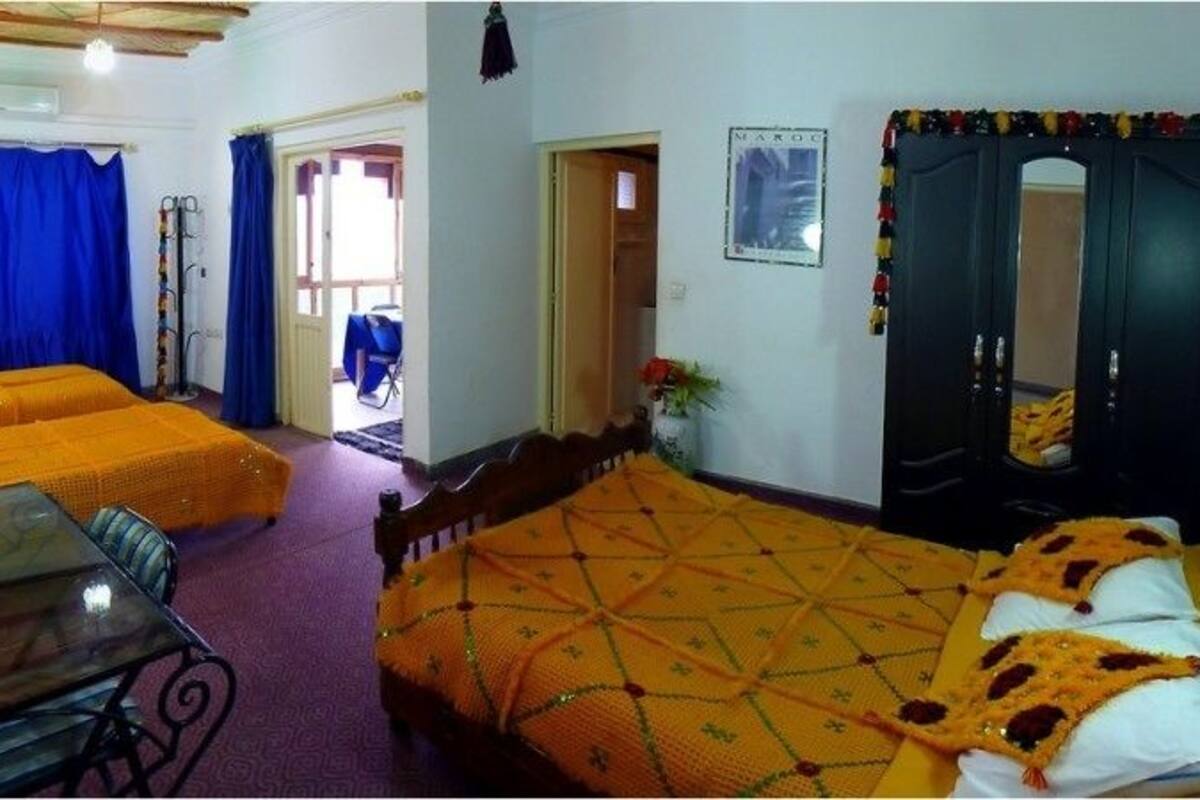 A room with two beds, a desk, and a chair. There is a window with blue curtains and a door with a mirror and decorations.