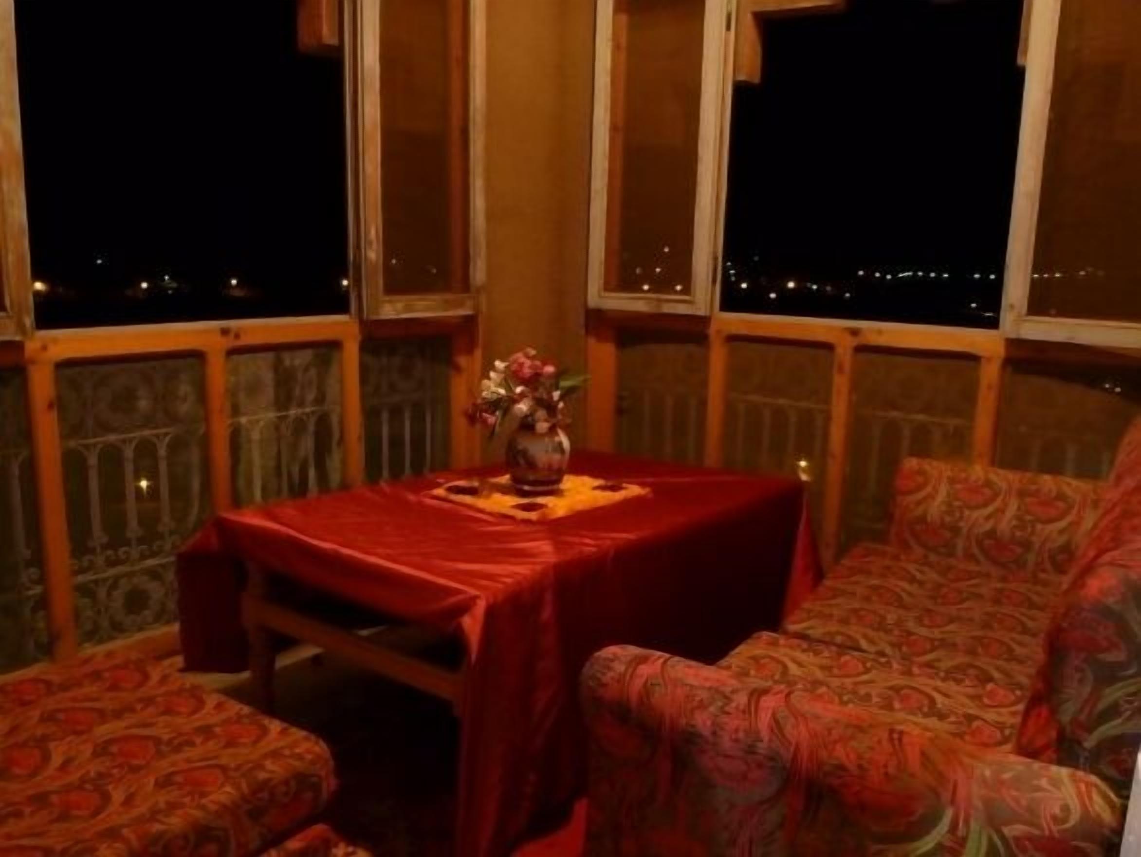 A balcony with a table and a sofa, a vase with flowers, and a city view at night.